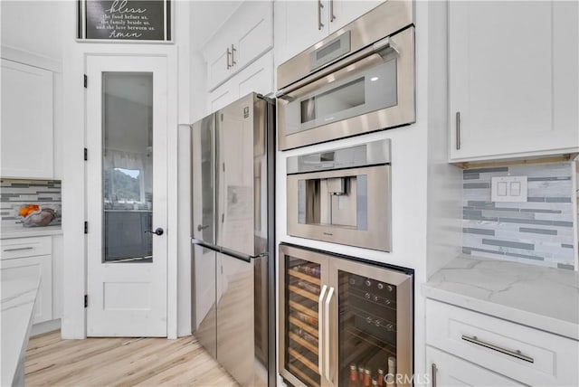 kitchen featuring white cabinetry, stainless steel appliances, beverage cooler, and light hardwood / wood-style flooring