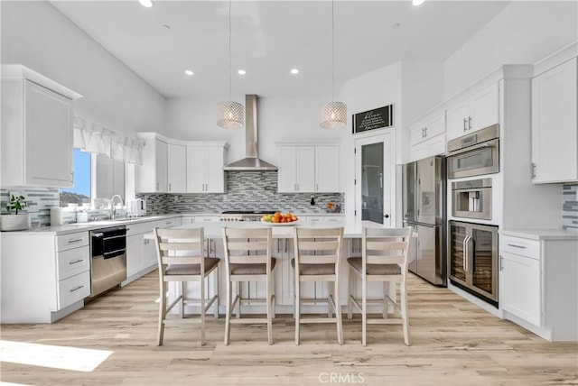 kitchen with a kitchen island, white cabinets, wall chimney range hood, and appliances with stainless steel finishes