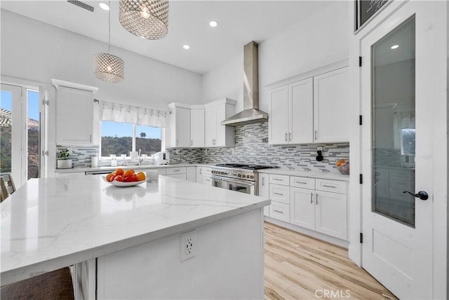 kitchen with white cabinets, pendant lighting, high end stainless steel range oven, and wall chimney exhaust hood