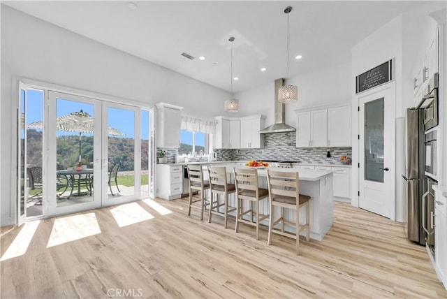 kitchen featuring white cabinetry, a center island, wall chimney exhaust hood, pendant lighting, and light hardwood / wood-style floors