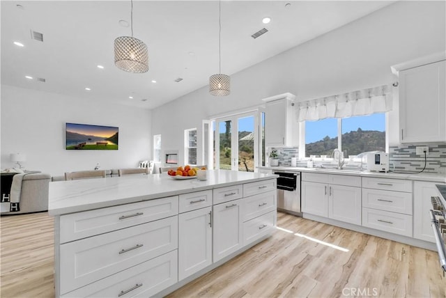 kitchen with backsplash, stainless steel dishwasher, sink, pendant lighting, and white cabinetry