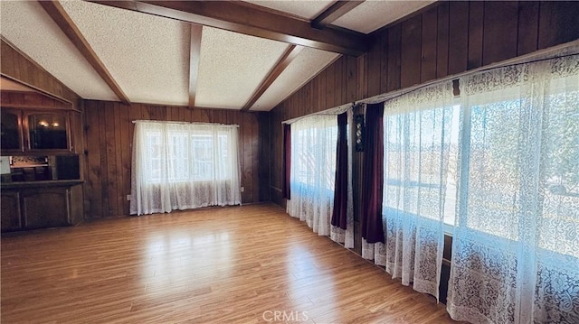 spare room featuring lofted ceiling with beams, light wood finished floors, a textured ceiling, and wooden walls