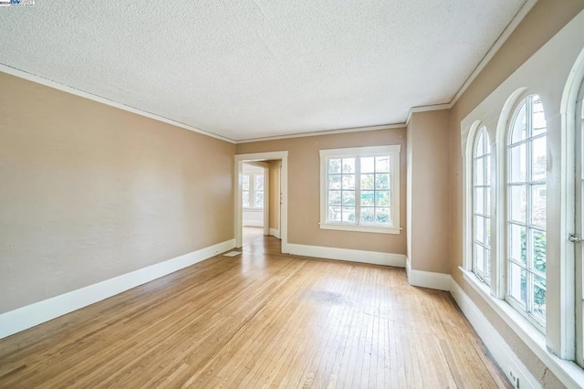 empty room with a healthy amount of sunlight, crown molding, and light hardwood / wood-style floors