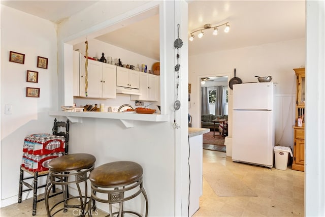 kitchen with kitchen peninsula, white cabinetry, a kitchen bar, and white refrigerator