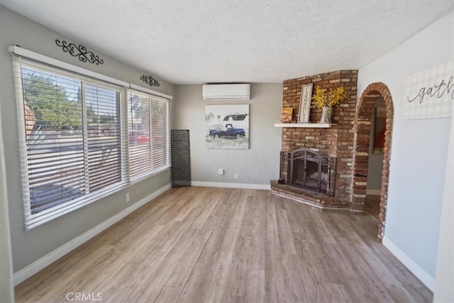 unfurnished living room featuring a textured ceiling, wood-type flooring, a wall mounted air conditioner, and a brick fireplace