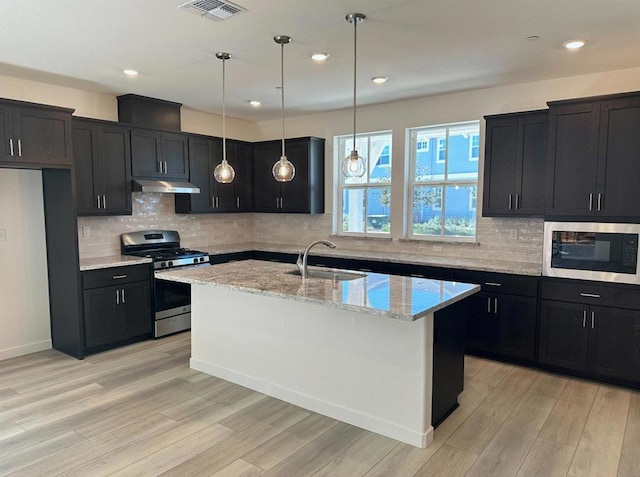 kitchen with gas stove, sink, a kitchen island with sink, light stone countertops, and built in microwave