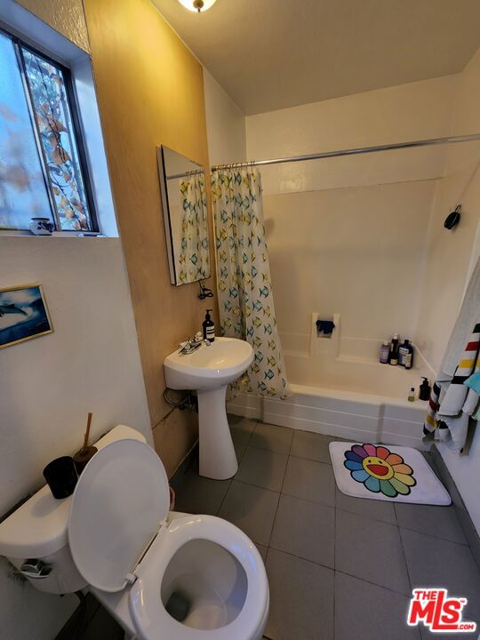 bathroom featuring toilet, shower / bathtub combination with curtain, and tile patterned floors