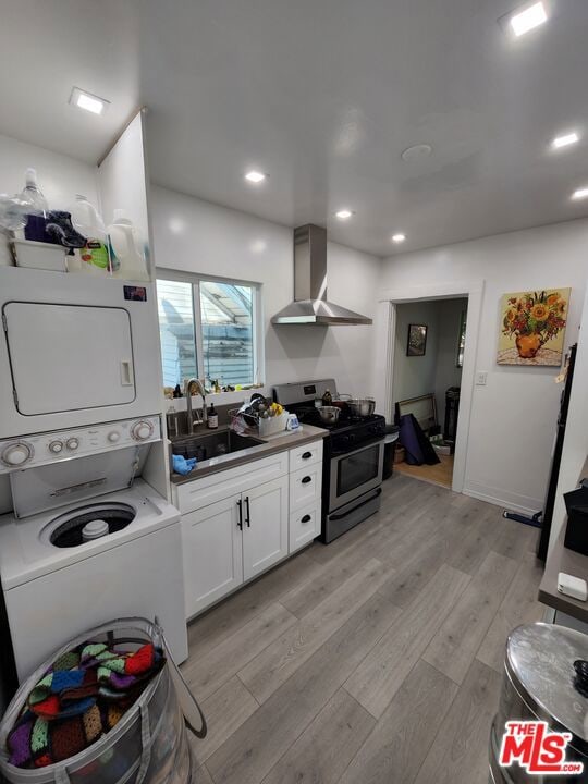 kitchen featuring white cabinetry, wall chimney exhaust hood, stacked washer / drying machine, light hardwood / wood-style flooring, and stainless steel range