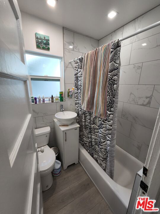 full bathroom featuring tile walls, wood-type flooring, shower / bath combo, vanity, and toilet