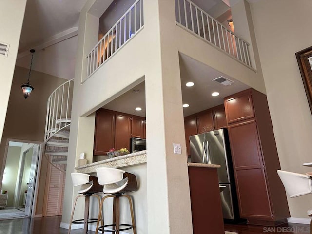 kitchen featuring light stone counters, dark hardwood / wood-style floors, stainless steel appliances, a breakfast bar, and a high ceiling