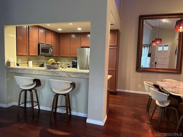 kitchen with dark hardwood / wood-style flooring, a breakfast bar, vaulted ceiling, hanging light fixtures, and appliances with stainless steel finishes