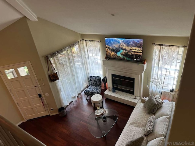 living room featuring dark hardwood / wood-style floors, lofted ceiling with beams, and a tile fireplace