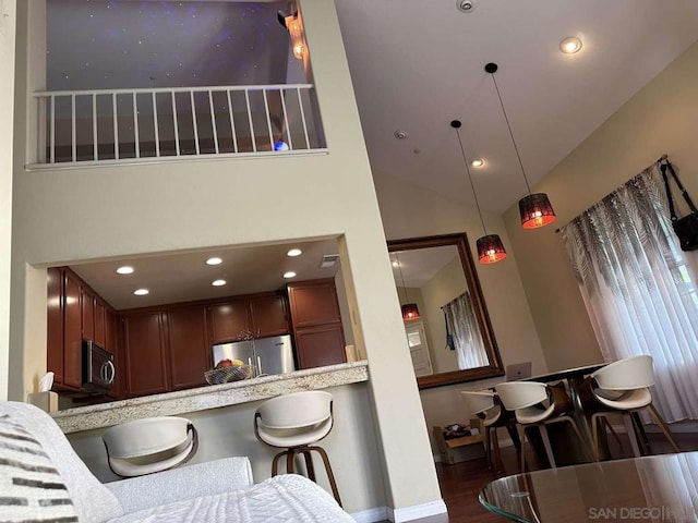 kitchen with stainless steel appliances, a breakfast bar, dark wood-type flooring, kitchen peninsula, and decorative light fixtures