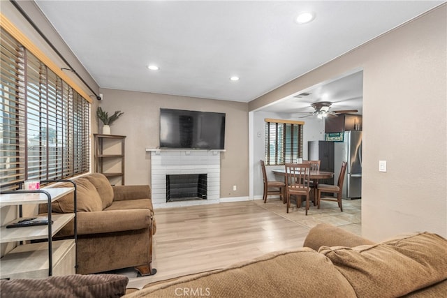 living room featuring a brick fireplace, light hardwood / wood-style floors, and ceiling fan