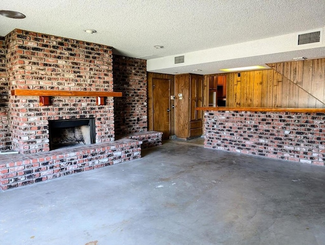 unfurnished living room featuring a textured ceiling, wood walls, concrete floors, and a brick fireplace