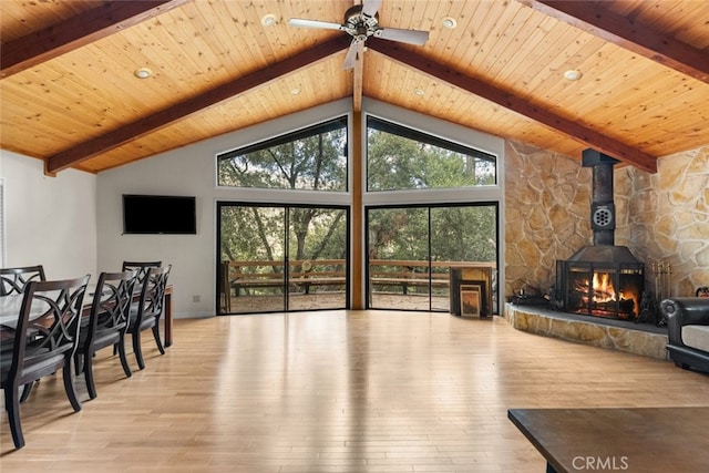 living room with beamed ceiling, ceiling fan, a wood stove, wooden ceiling, and light hardwood / wood-style flooring