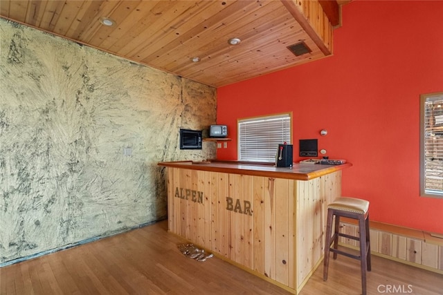 bar with light brown cabinets, wood ceiling, and light hardwood / wood-style flooring