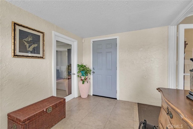 entryway with light tile patterned floors, a textured wall, and a textured ceiling