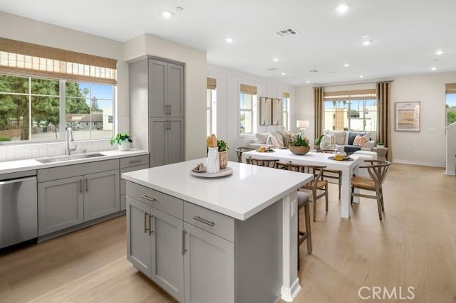 kitchen featuring light wood-type flooring, stainless steel dishwasher, sink, a center island, and gray cabinets