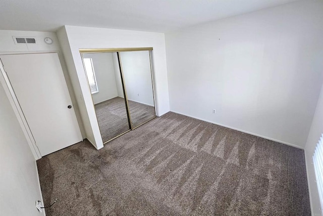 unfurnished bedroom with dark colored carpet and a closet