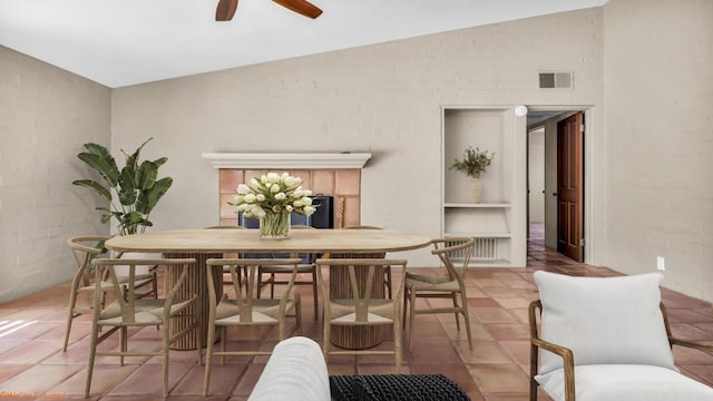 dining room with ceiling fan, lofted ceiling, light tile patterned floors, and a tiled fireplace