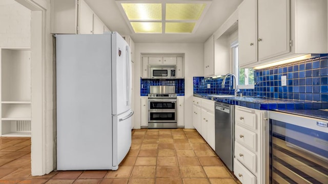 kitchen featuring decorative backsplash, stainless steel appliances, beverage cooler, tile countertops, and white cabinetry