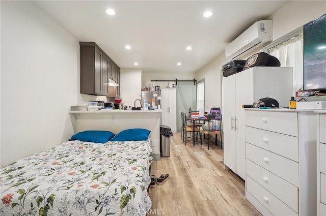 bedroom featuring an AC wall unit, stainless steel fridge, light hardwood / wood-style flooring, and a barn door