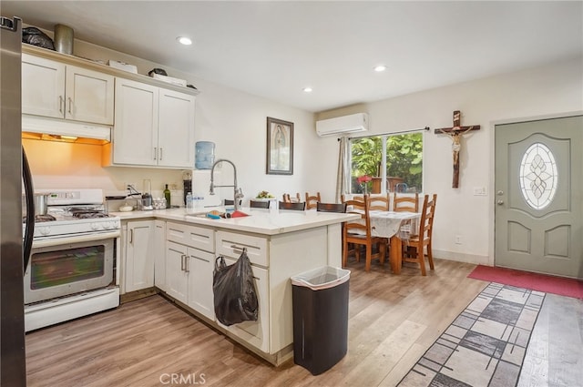 kitchen with white range with gas stovetop, kitchen peninsula, light wood-type flooring, sink, and a wall mounted air conditioner