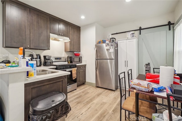 kitchen featuring light hardwood / wood-style floors, a barn door, stainless steel appliances, dark brown cabinetry, and sink