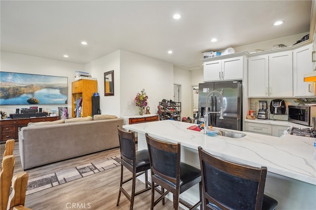 kitchen featuring a kitchen breakfast bar, refrigerator with ice dispenser, white cabinetry, and light stone counters