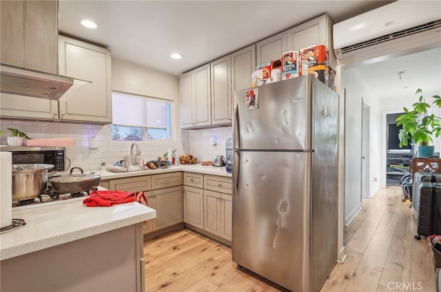 kitchen with tasteful backsplash, sink, light hardwood / wood-style flooring, appliances with stainless steel finishes, and a wall mounted AC