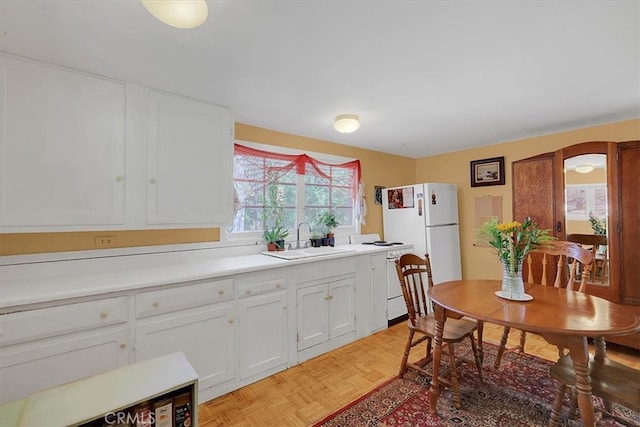 kitchen with light parquet flooring, white appliances, sink, and white cabinetry