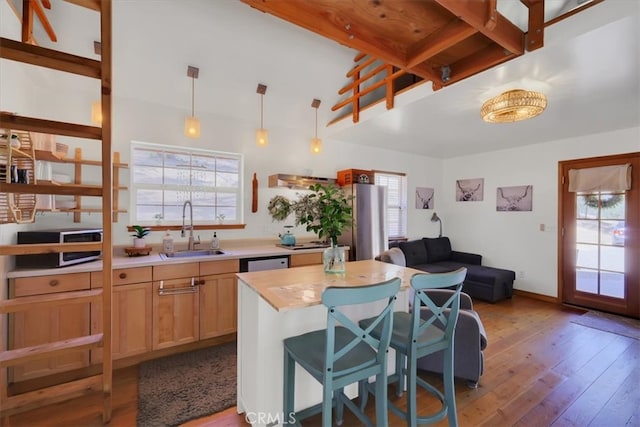 kitchen with hanging light fixtures, sink, a kitchen island, a breakfast bar area, and light hardwood / wood-style floors