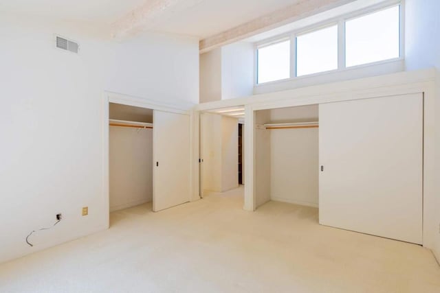 unfurnished bedroom featuring light carpet, beam ceiling, and multiple closets