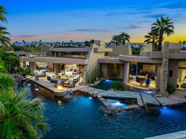 back house at dusk featuring a water view, a patio area, pool water feature, and a pool with hot tub