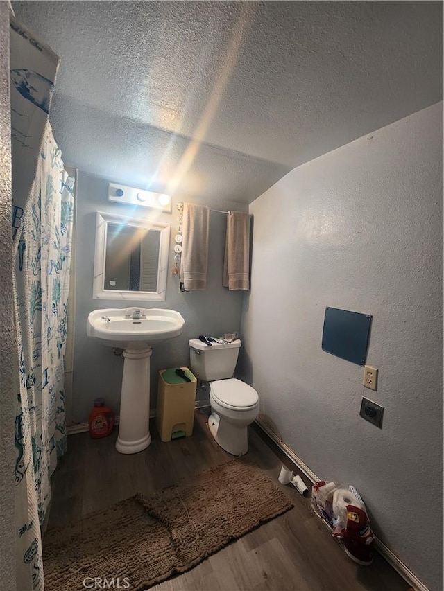 bathroom with vaulted ceiling, sink, hardwood / wood-style flooring, toilet, and a textured ceiling