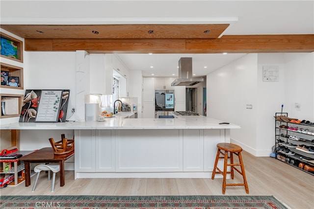 kitchen featuring beam ceiling, light wood-type flooring, island range hood, white cabinetry, and light stone counters