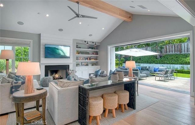 living room featuring ceiling fan, a fireplace, lofted ceiling with beams, light wood-type flooring, and built in shelves