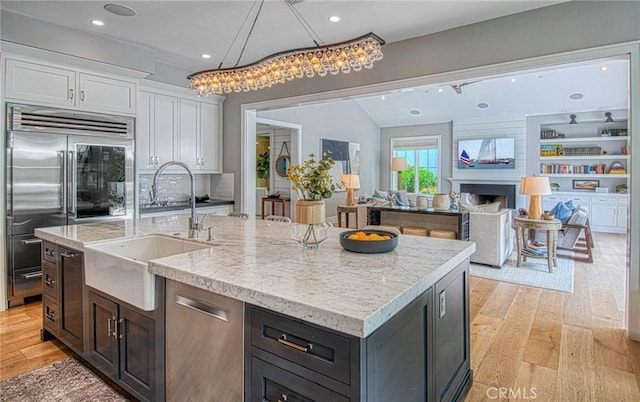 kitchen with sink, appliances with stainless steel finishes, a kitchen island with sink, light hardwood / wood-style floors, and white cabinets