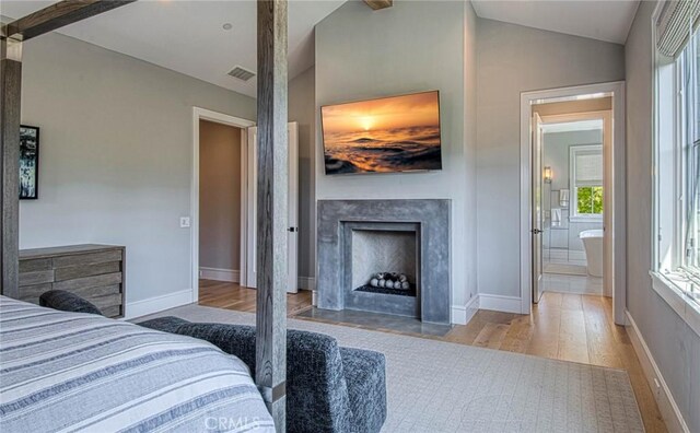 bedroom with vaulted ceiling with beams, light wood-type flooring, and connected bathroom