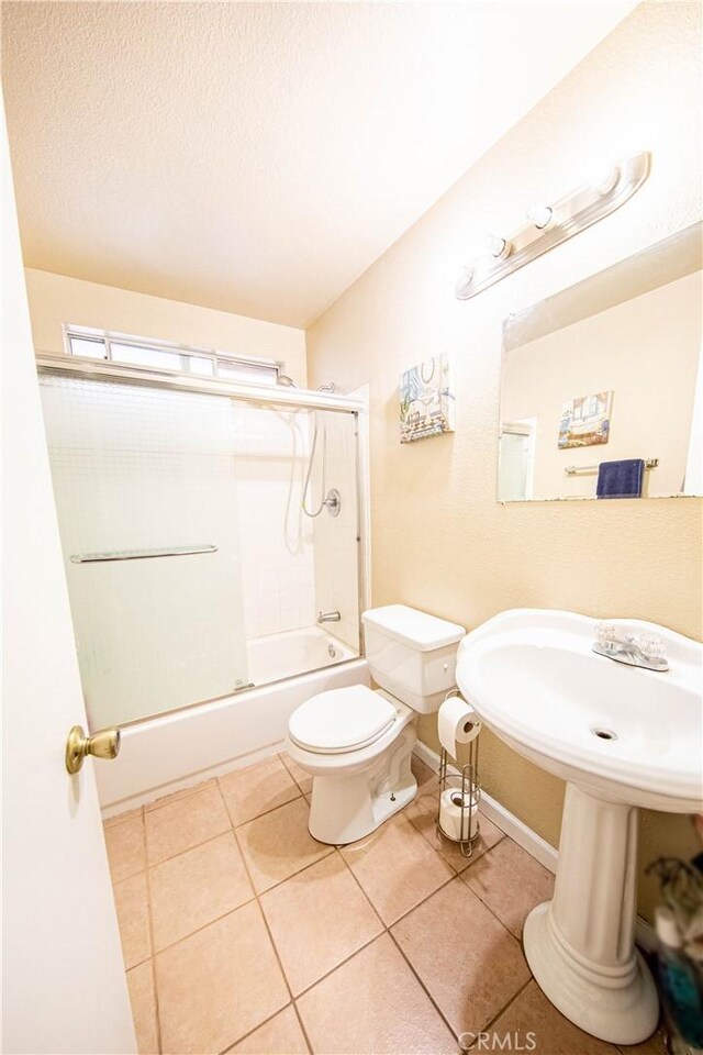 full bathroom featuring bath / shower combo with glass door, sink, tile patterned flooring, and toilet