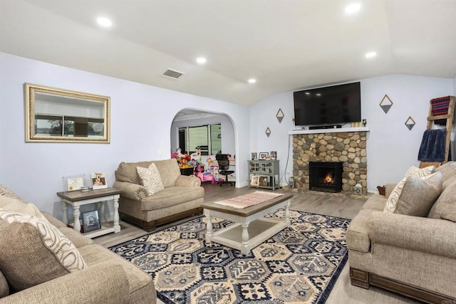 living room featuring a stone fireplace, vaulted ceiling, and light wood-type flooring