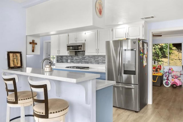 kitchen featuring a kitchen breakfast bar, stainless steel appliances, a center island, tasteful backsplash, and white cabinets