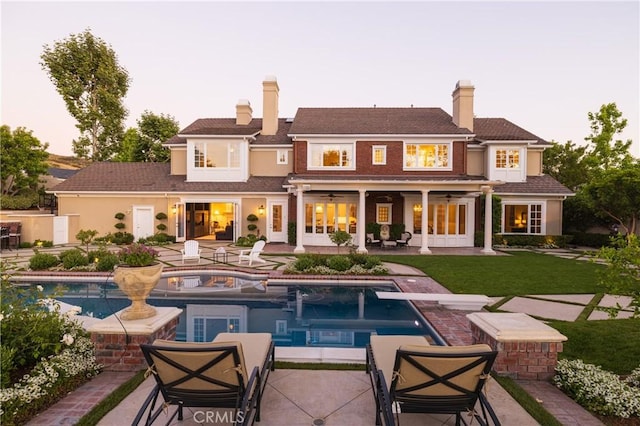 back house at dusk with ceiling fan, a swimming pool with hot tub, a patio area, and a yard