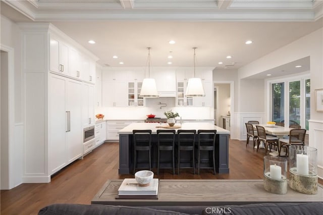 kitchen featuring a breakfast bar area, white cabinetry, a center island with sink, and crown molding