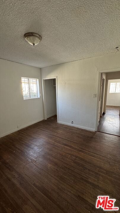 empty room featuring a textured ceiling, dark wood-type flooring, and a healthy amount of sunlight