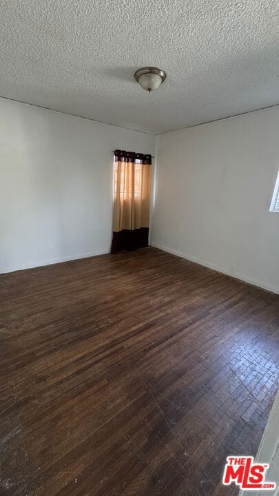 empty room with plenty of natural light, a textured ceiling, and dark hardwood / wood-style flooring