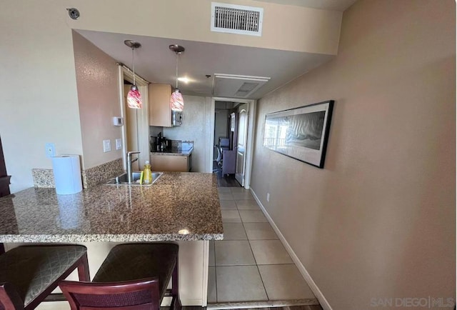 kitchen featuring pendant lighting, light tile patterned floors, sink, kitchen peninsula, and a kitchen bar