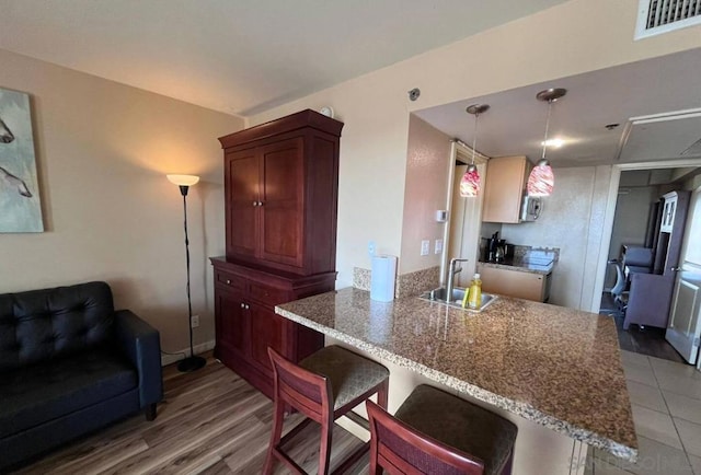 kitchen with light hardwood / wood-style floors, sink, kitchen peninsula, a kitchen bar, and decorative light fixtures