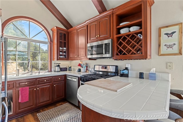 kitchen with kitchen peninsula, sink, stainless steel appliances, lofted ceiling with beams, and tile counters